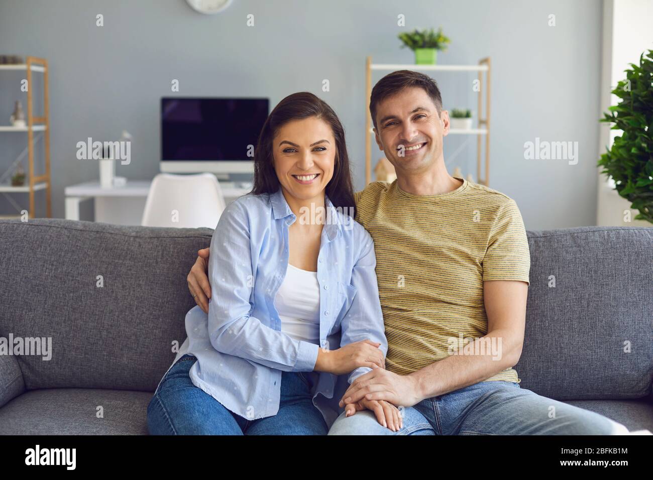 Ein positives Paar umarmt Blick auf die Kamera während auf einem Sofa im Innenraum des Hauses sitzen. Stockfoto