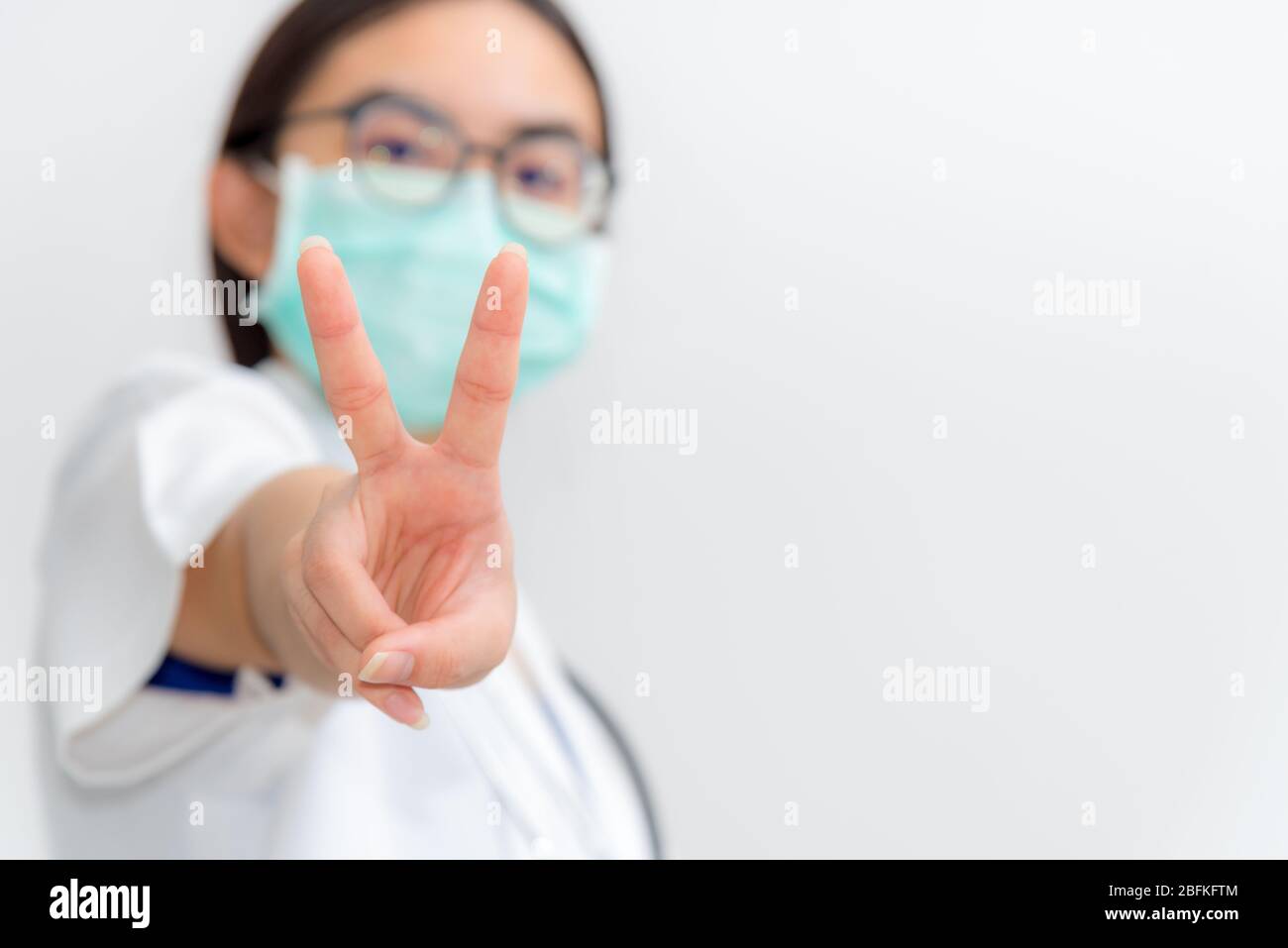 Studio Portrait Asiatische junge Frau Arzt Nahaufnahme Raise zwei V-Form Finger Tragen Sie eine Maske zur Sicherheit Coronavirus im Kampf gegen Krankheit ep zu unterstützen Stockfoto