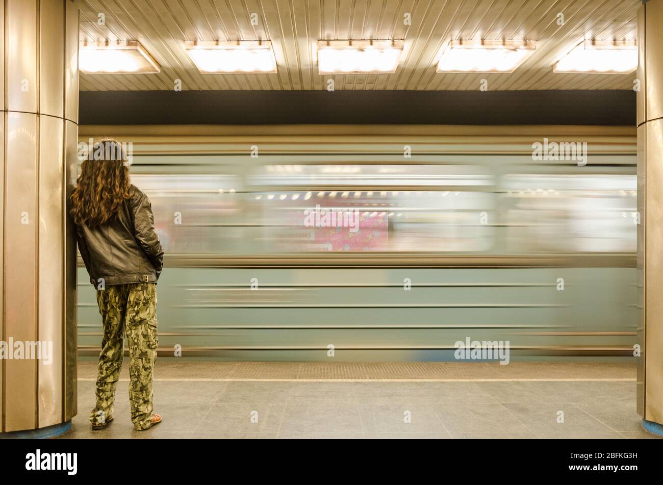 Rückansicht eines langhaarigen Mannes, der einen U-Bahn-Zug an der U-Bahn-Station Deák Ferenc tér in Budapest, Ungarn vorbeifährt Stockfoto