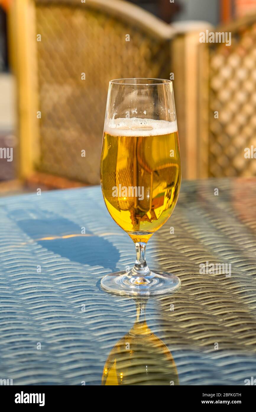 Glas goldenes Bierlager auf der Glastisch-Tischplatte der Gartenmöbel Stockfoto