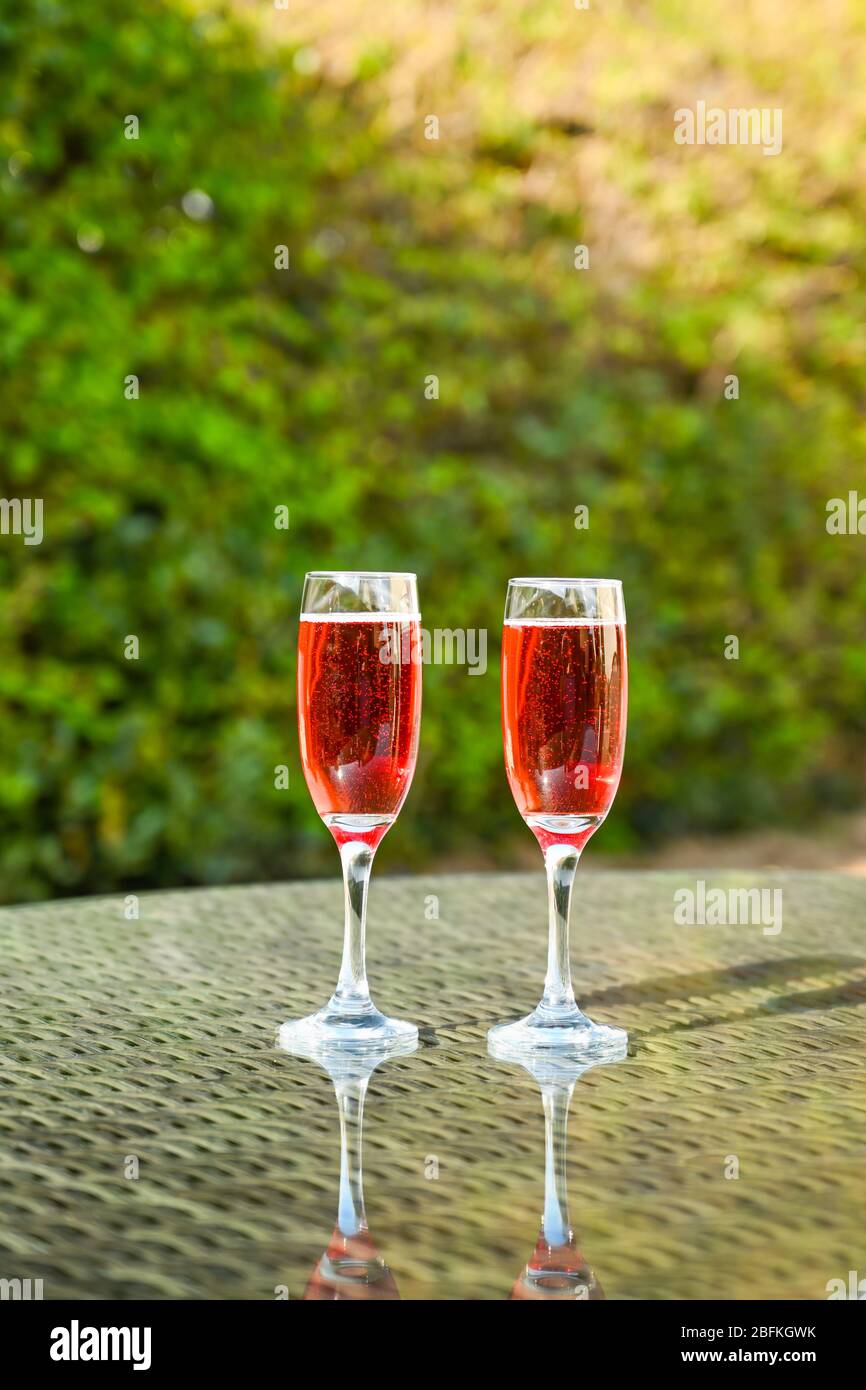 Rosa Champagner in zwei Flötengläsern nebeneinander auf einer Glastisch-Platte im Garten Stockfoto