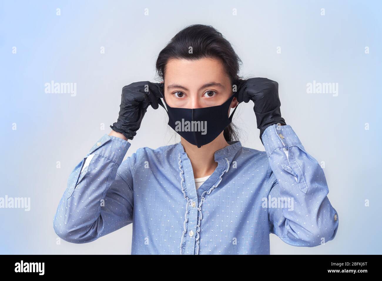 Das Mädchen in Handschuhen zieht eine medizinische Maske an. Prävention von Viruserkrankungen der Erkältung und Grippe. Hellgrau-blauer Hintergrund. In einer Atemmaske. Stockfoto