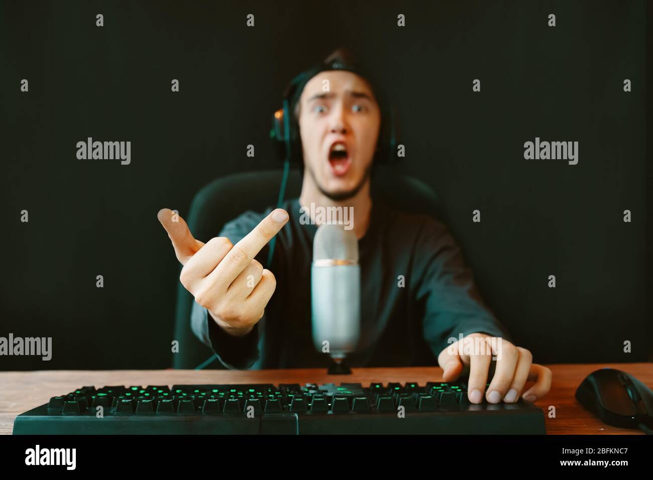Gamer Online Streamer mit Mikrofon, Tastatur am Computer zeigt den  Mittelfinger. Der Mann ist mit dem Spiel unzufrieden Stockfotografie - Alamy