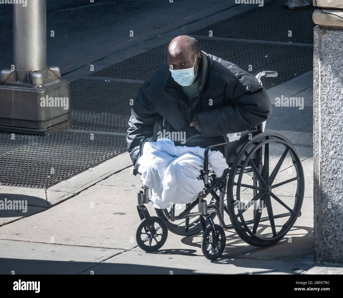 New York, USA. April 2020. Ein obdachloser Bettler mit Gesichtsmaske positioniert seinen Rollstuhl in einer Straßenecke in New York City. Die Regierung erklärte, dass Newyorker ihre Gesichter bedecken sollten, wenn sie nach draußen gehen und keine soziale Distanz einpflegen können, um die Ausbreitung des Coronavirus zu verhindern. Kredit: Enrique Shore/Alamy Live News Stockfoto