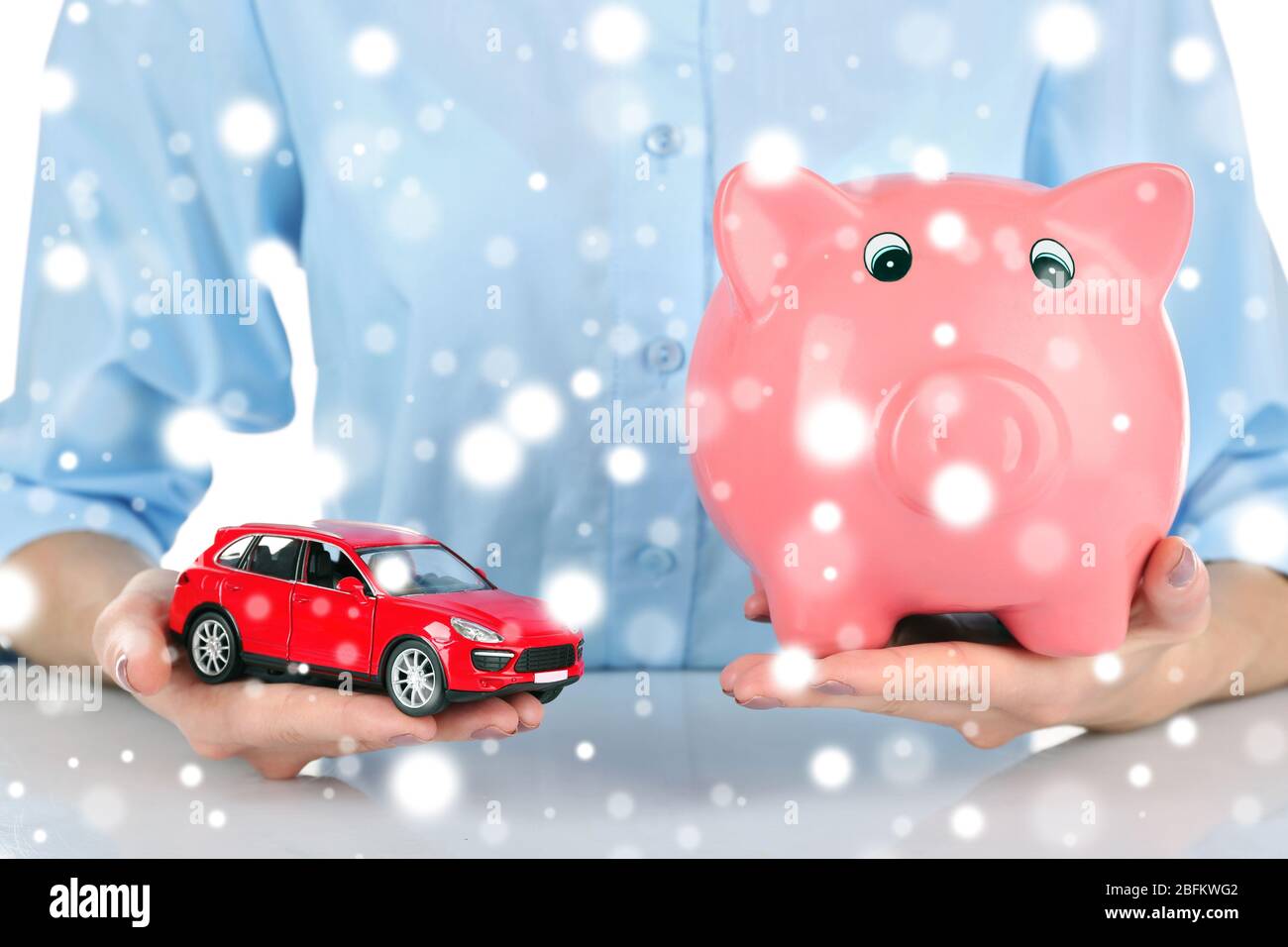 Weibliche Hände halten Sparschwein und Modell des Autos über Schnee-Effekt Stockfoto