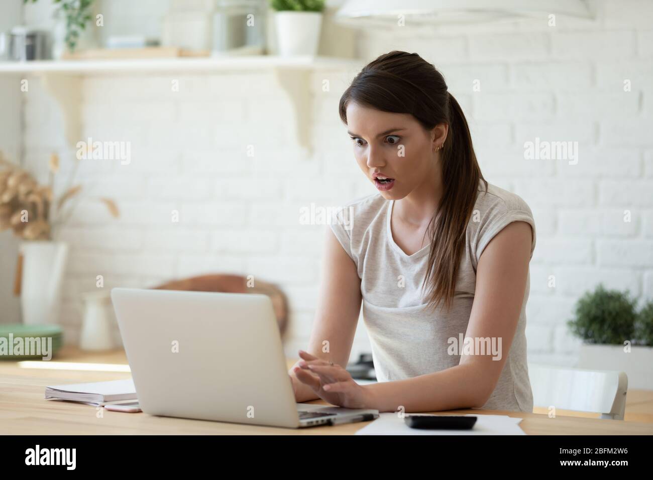 Schockierende junge Frau mit Rechner und Laptop für die Berechnung der Finanzen. Stockfoto