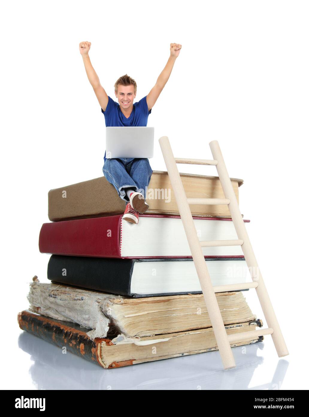 Schöner junger Mann mit Laptop auf Stapel von Büchern auf weiß isoliert sitzen Stockfoto