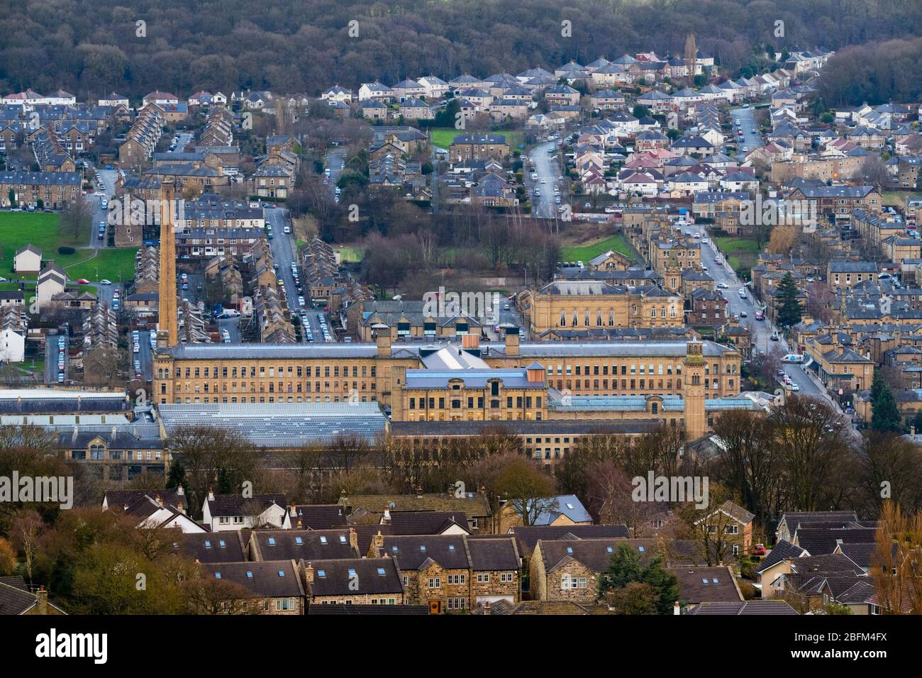 Historische beeindruckende viktorianische Textilfabrik (Kunstgalerie) im Aire-Tal, hoher Kamin, der über den Häusern thront - Salts Mill, Saltaire, Bradford England, Großbritannien Stockfoto