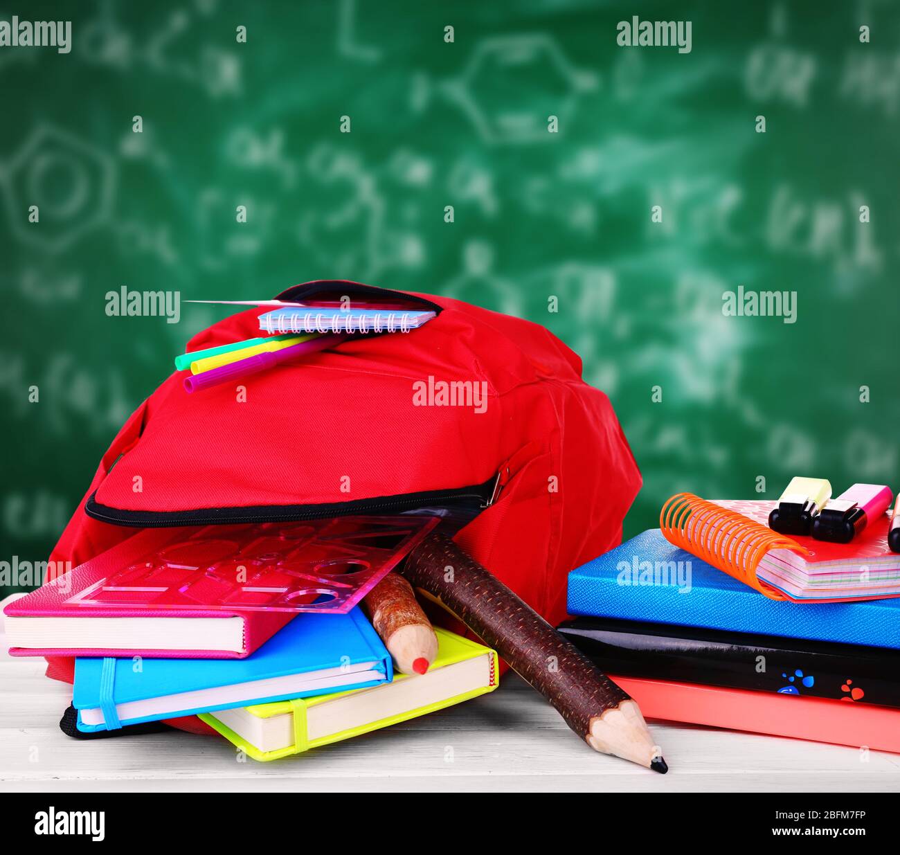 Rote Tasche mit Schulausrüstung auf Holztisch neben Tafel Stockfoto