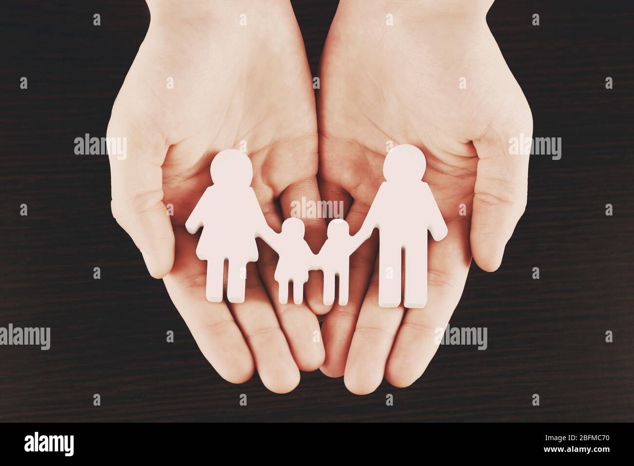 Weibliche Hände mit Familienmodell auf dunklem Holzhintergrund Stockfoto