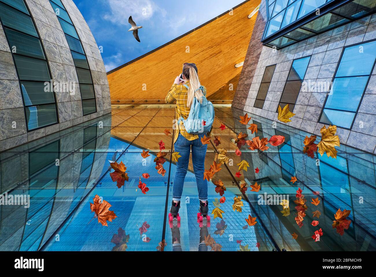Perspektive. Ein konzeptuelles Foto einer weiblichen Rollerin, die ein Bürogebäude hochfährt, während sie eine Möwe fotografiert, mit hinterhängenden Blättern Stockfoto