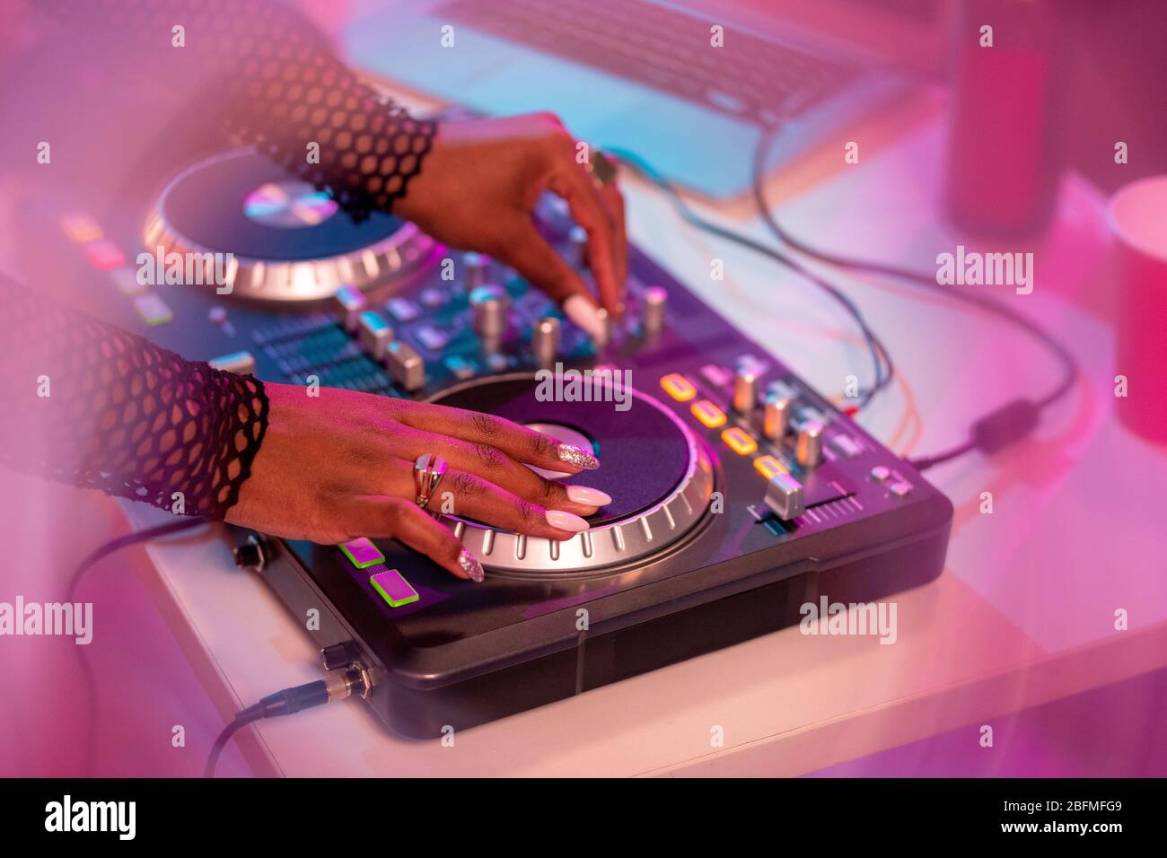 Hände afrikanischer weiblicher Deejay bewegen Drehscheibe, während sie am Schreibtisch stehen und Klänge mischen und neue Musik für Disco-Tanz machen Stockfoto