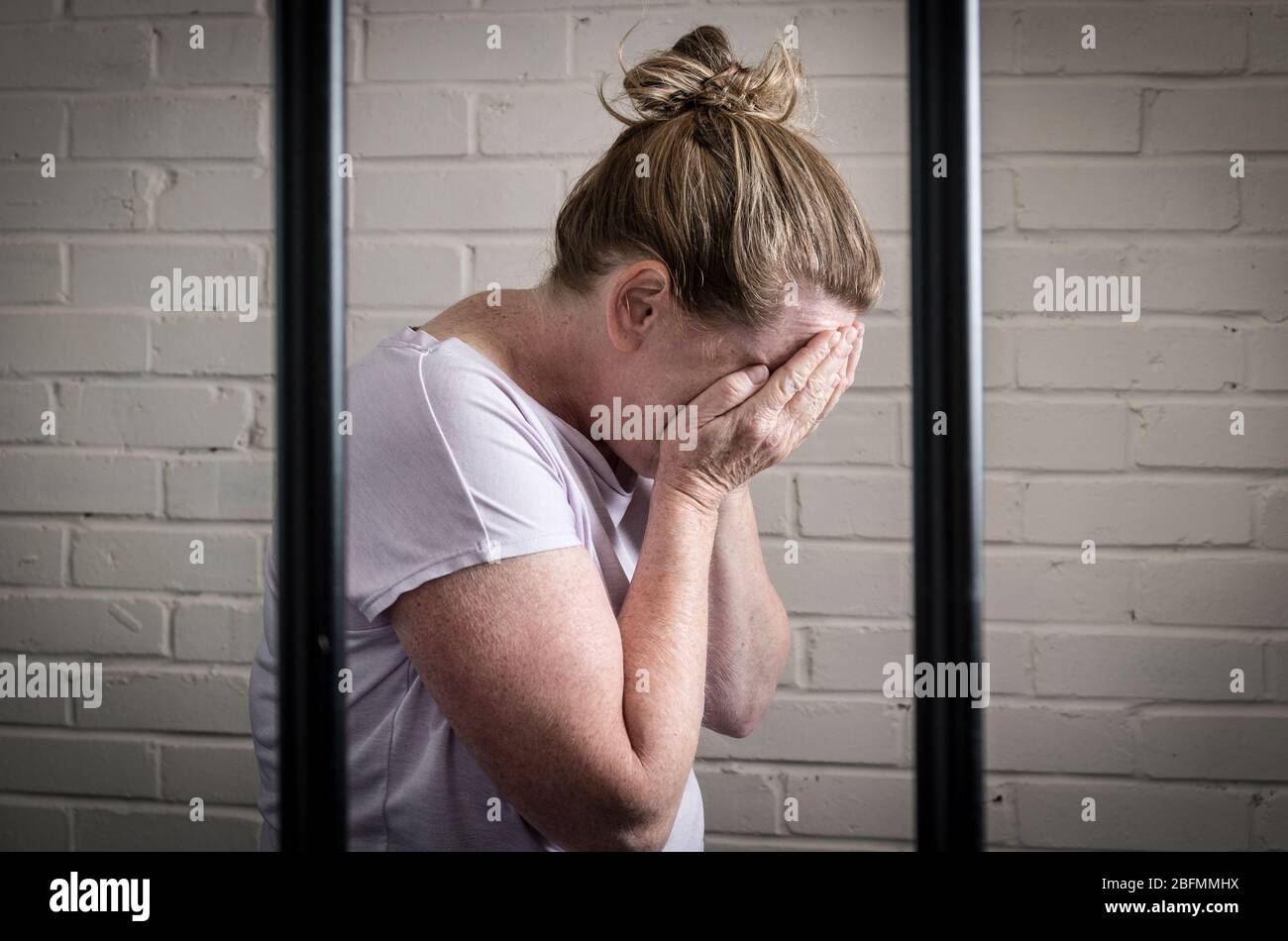 Eine traurige, verärgerte weibliche Gefangene hinter Gittern in einem Frauengefängnis. Bild nach Modell gestellt. Stockfoto