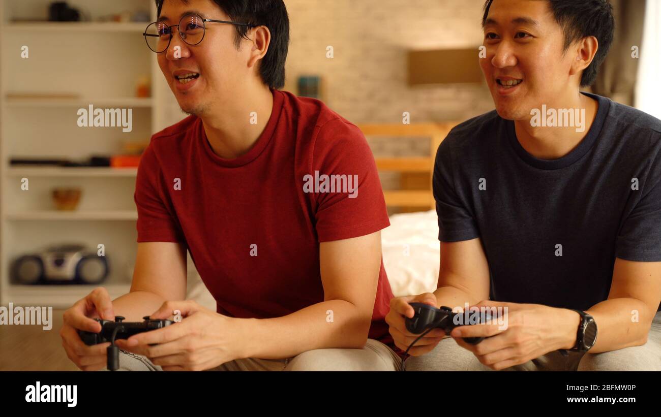 Junge männliche Freunde spielen Spiel mit Joystick zu Hause. Asiatische Männer Fernsehen Videospiel zusammen zu spielen. Stockfoto