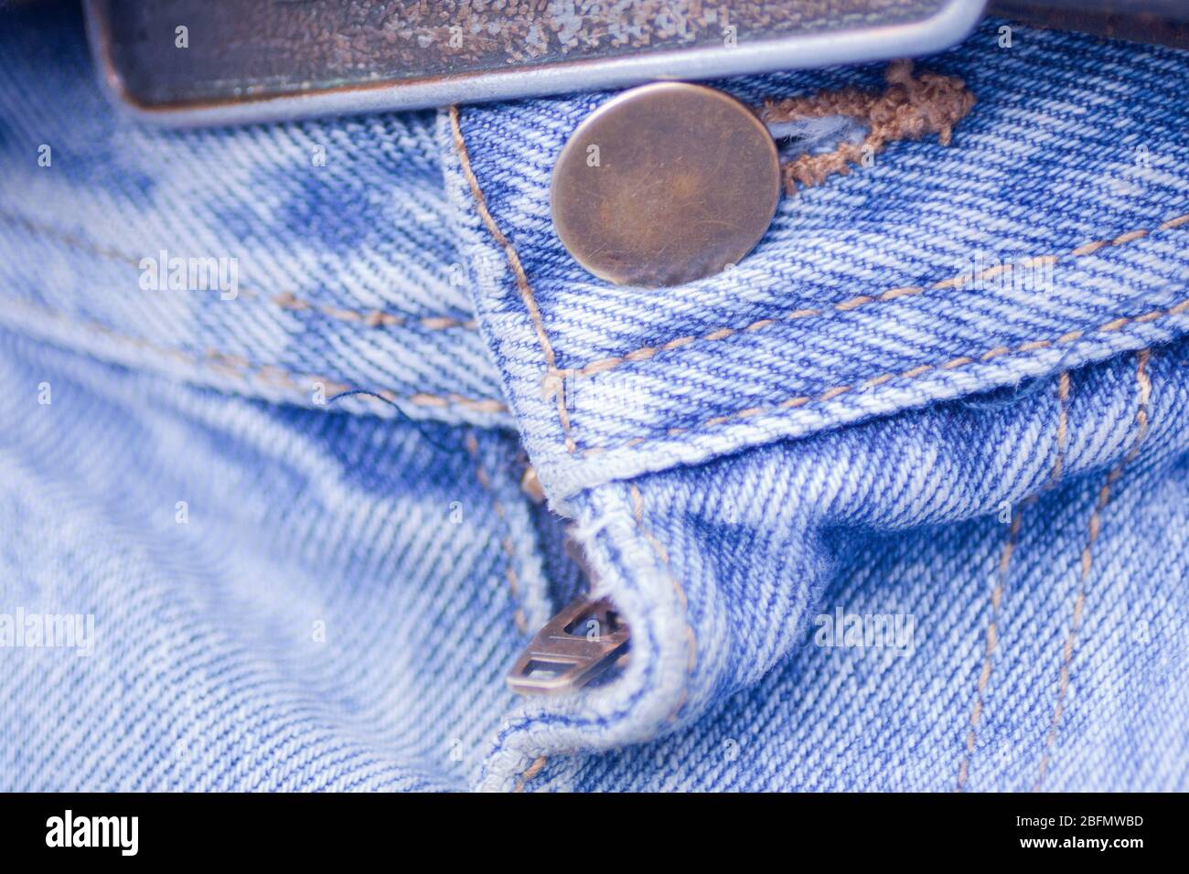 Schließen Sie eine Gürtelschnalle, Knopf und Reißverschluss der blauen Jeans. Makro-Ansicht von Knopf, Reißverschluss und Textur von verblichenem blauen Denim-Stoff. Stockfoto
