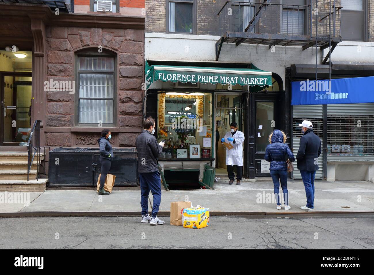 Menschen sozialen Distanzen und tragen Masken, wie sie warten, um eine Metzgerei während Coronavirus COVID-19 betreten. New York, 18. April 2020. Stockfoto