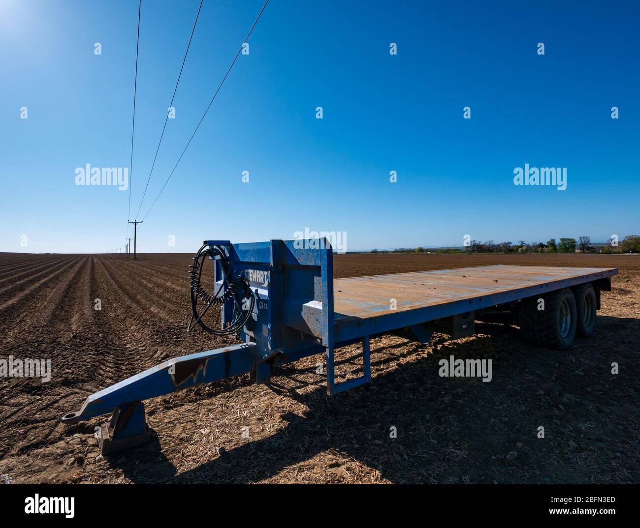 Landwirtschaftliche Anhänger in gepflügten Feld und Stromkabel Pole, die in die Ferne, East Lothian, Schottland, Großbritannien Stockfoto