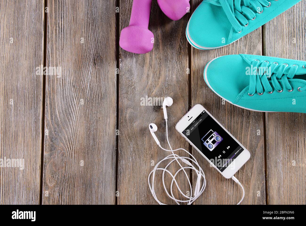 Weißes Smartphone mit Kopfhörer, rosa Glocken und Gumshoes auf Holzhintergrund Stockfoto