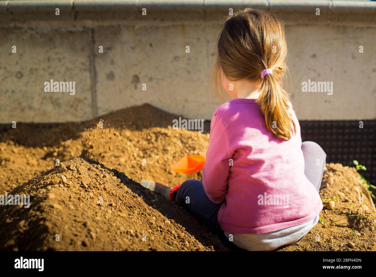 Kleines Mädchen, das während der Blockade der COVID-19-Pandemie mit einer Schaufel im Garten Erde gräbt. Outdoor-Aktivität Idee für Kinder während des Aufenthalts zu Hause. Stockfoto