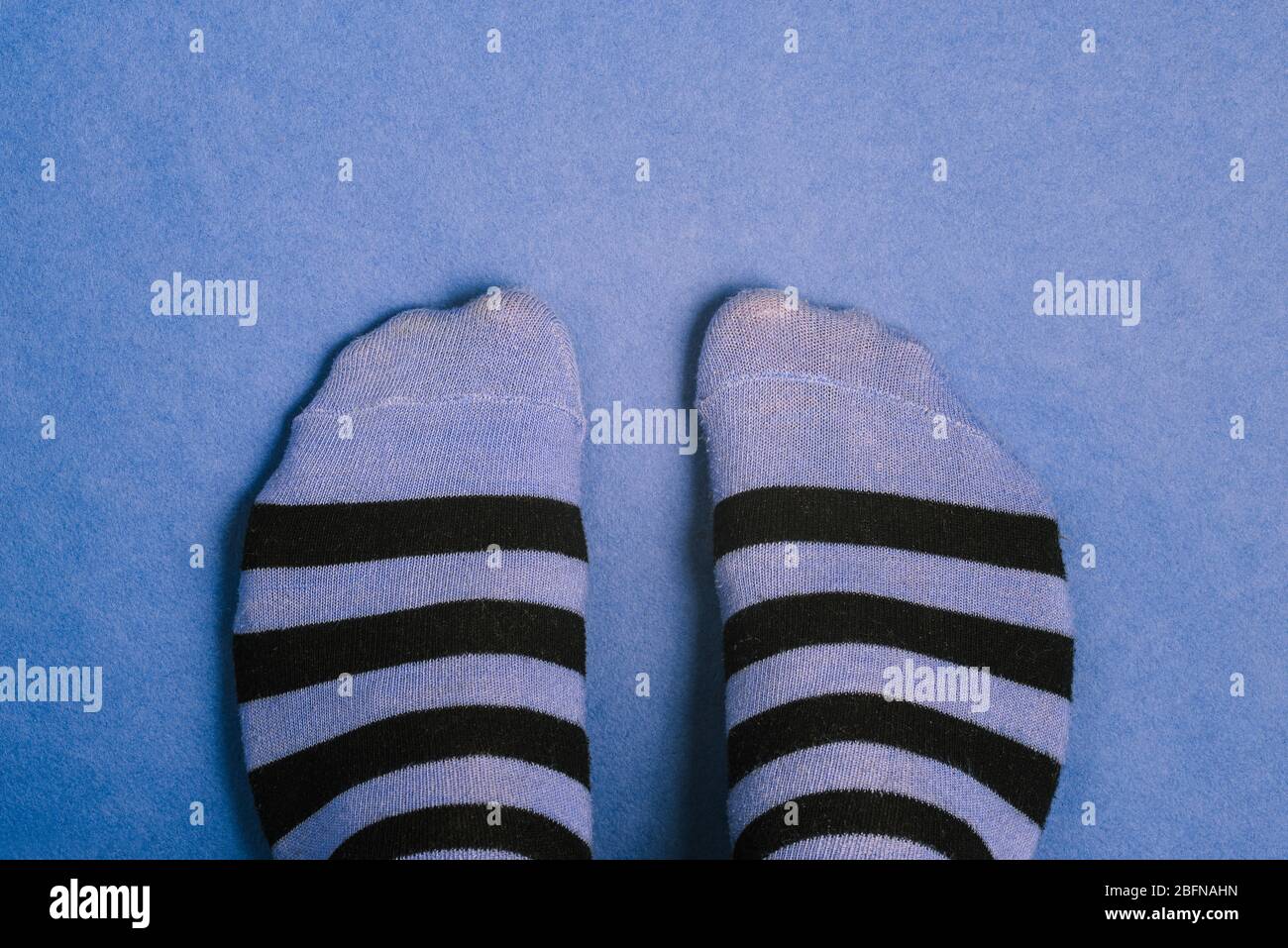 Gestreifte Socken auf blauem Hintergrund. Nahaufnahme von lustigen Socken. Schwarze und blaue Streifen. Draufsicht, Kopierbereich Stockfoto