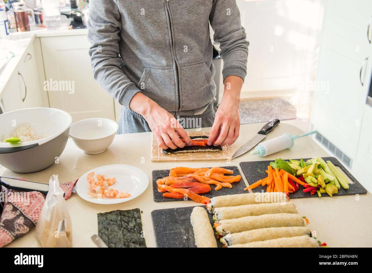 Kaukasischer Mann bereitet hausgemachte Sushi-Rollen. Sushi füllen. Die Schritte zum Erstellen von Sushi mit Lachs. Prozess der Sushi-Herstellung durch Nachkochen auf Stockfoto