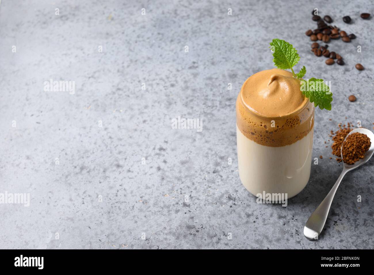 Dalgona schaumiriger Kaffee im Glas garnieren melissa auf grau. Trend koreanischen Eisgetränk mit Schaum von Instant-Kaffee. Nahaufnahme. Kopierbereich. Stockfoto