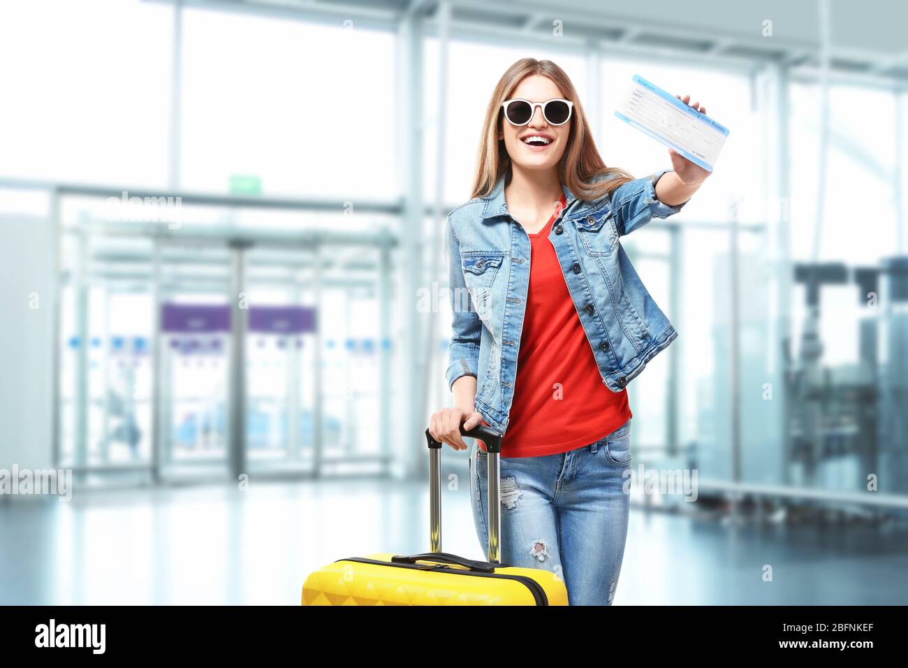 Junge Frau mit Ankunftskarte und Gepäck am Flughafen Stockfoto