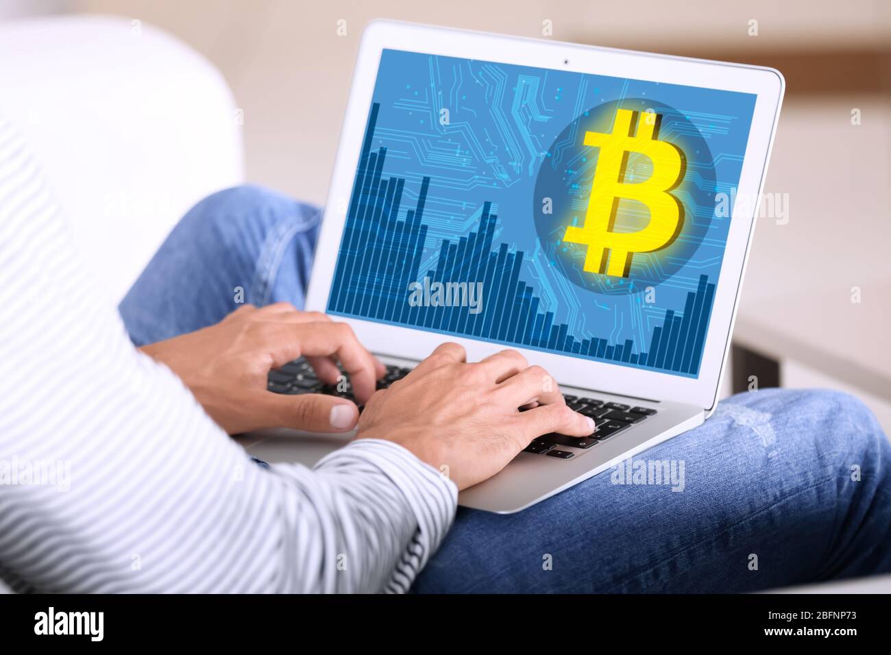 Mann, der Laptop mit Bitcoin-Symbol auf dem Bildschirm zu Hause Stockfoto