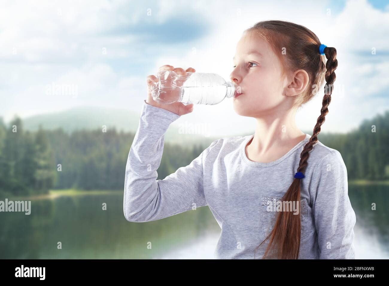 Kleines Mädchen mit Flasche sauberes Wasser auf Landschaftshintergrund Stockfoto