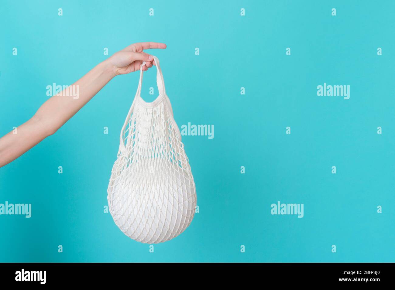 Weiße Netztasche mit Volleyball in der Hand auf blauem Hintergrund mit Kopierfläche. Stockfoto