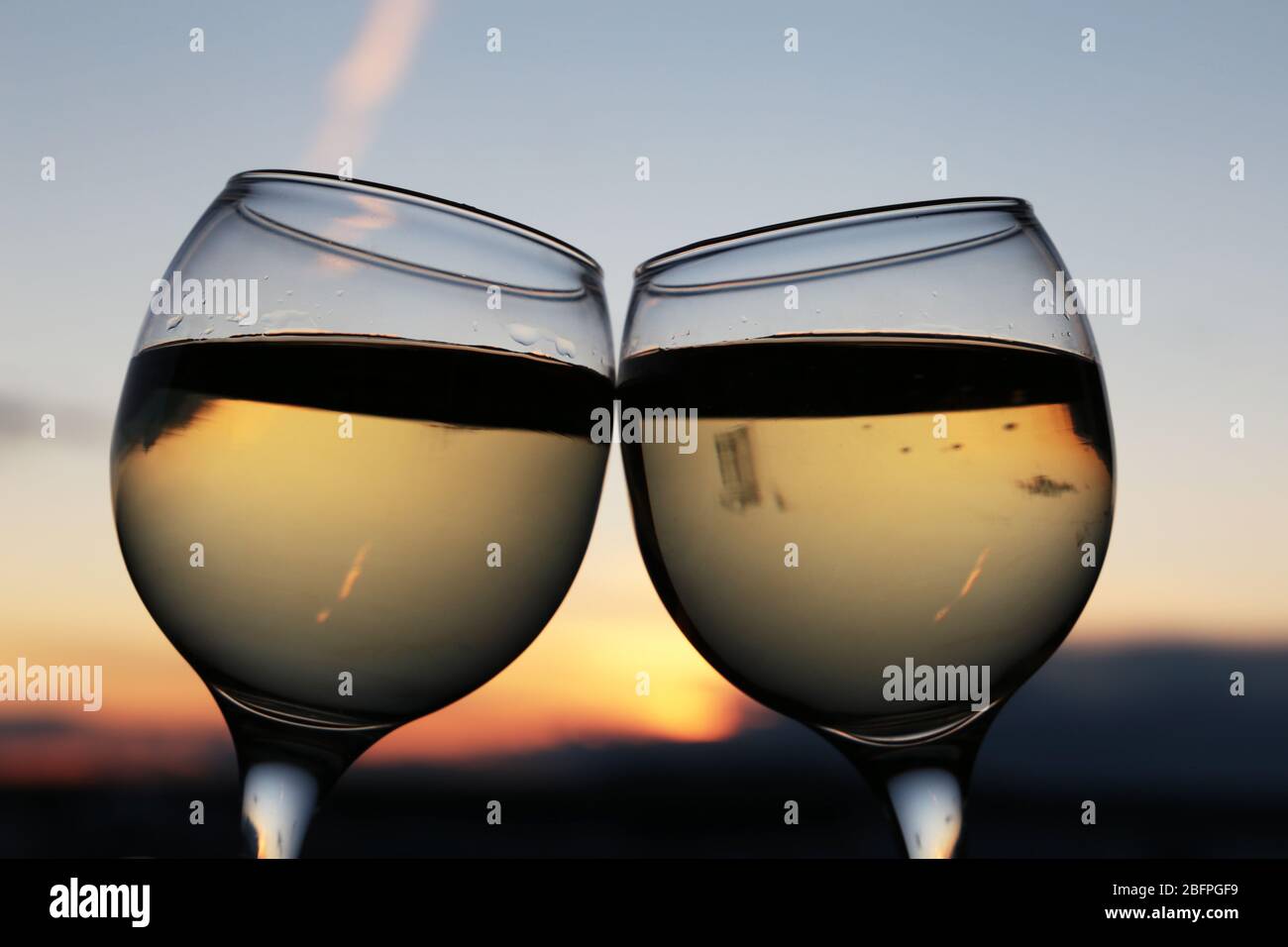 Zwei Gläser mit Weißwein auf buntem Sonnenuntergang Hintergrund. Paar klirren Gläser, Konzept der Feier, romantischen Abend zu Hause Quarantäne Stockfoto