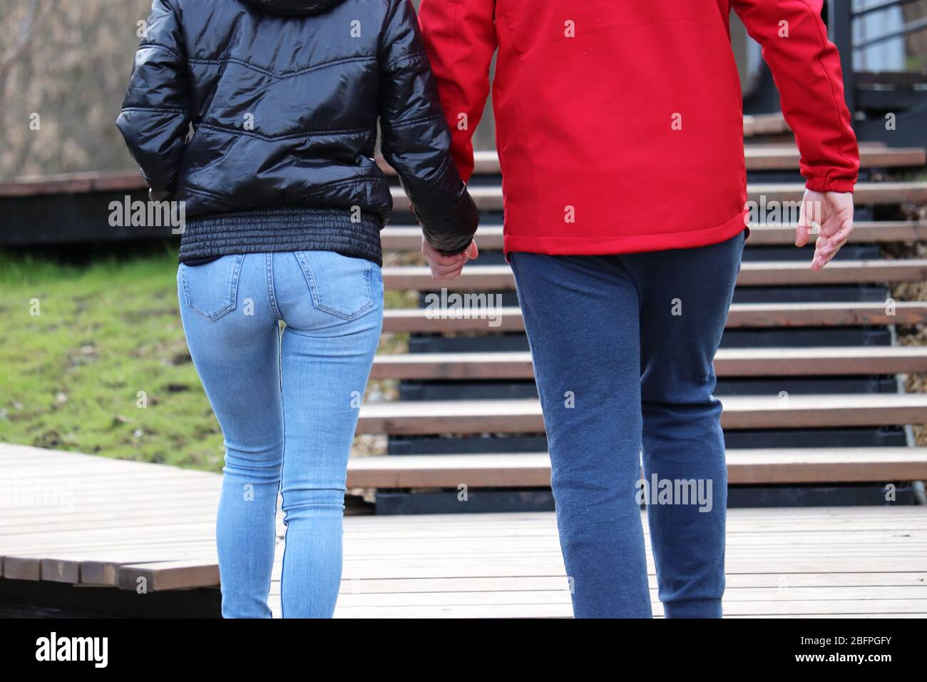 Paar in zwangloser Kleidung, die auf der Straße in einem Frühlingspark spazieren. Mann und Mädchen halten Hände, Konzept der Beziehung, romantisches Datum Stockfoto
