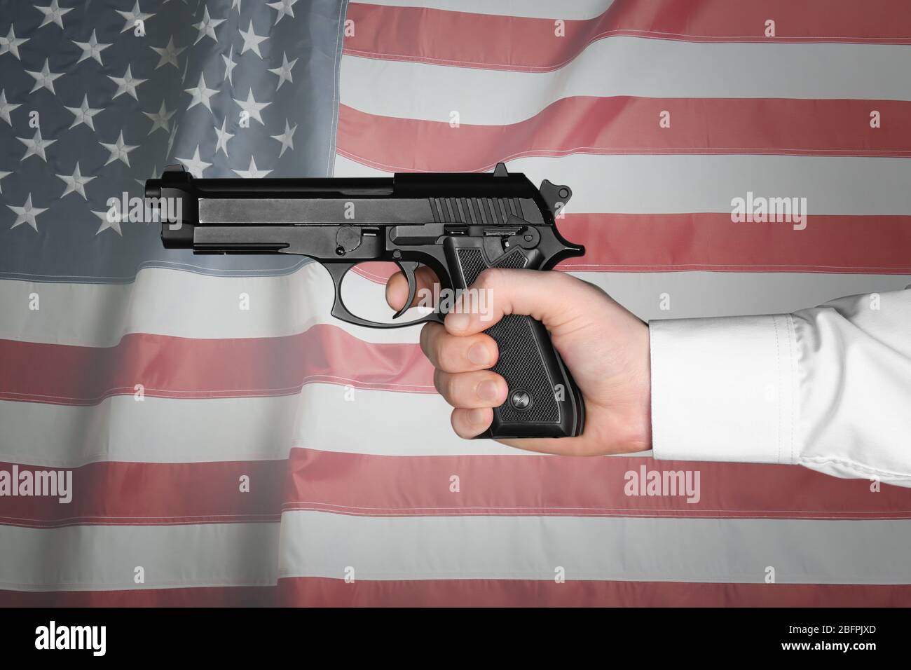 Mann mit Feuerwaffe und amerikanischer Flagge im Hintergrund. Konzept der Waffenkontrolle Stockfoto