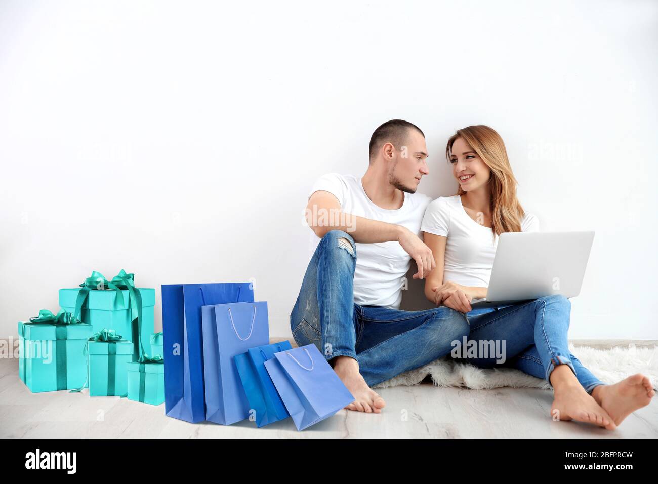 Internet-Shopping-Konzept. Junges Paar sitzt mit Laptop und Einkäufe in der Nähe der Wand zu Hause Stockfoto