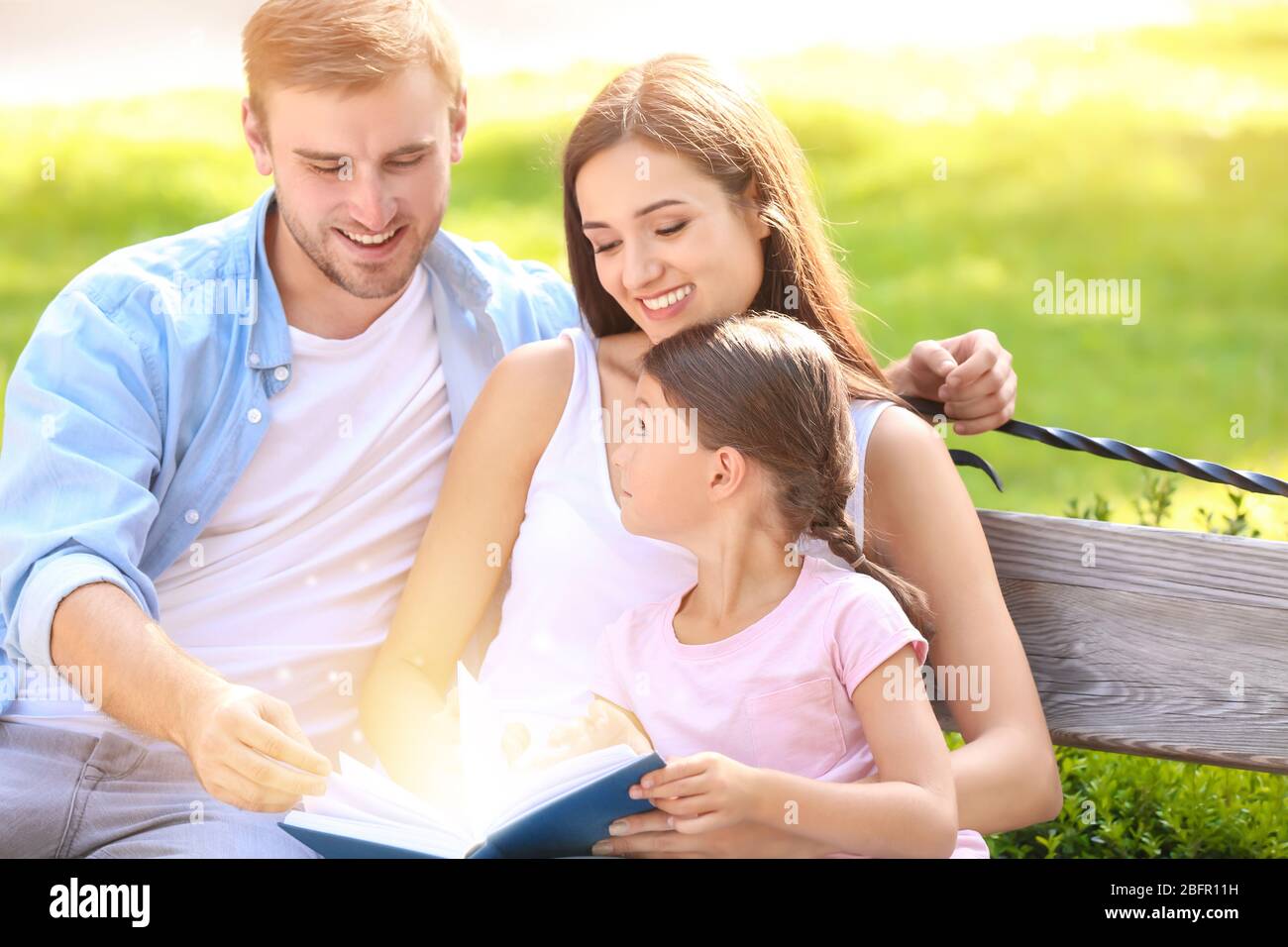 Eltern mit Tochter lesen Buch im Park Stockfoto