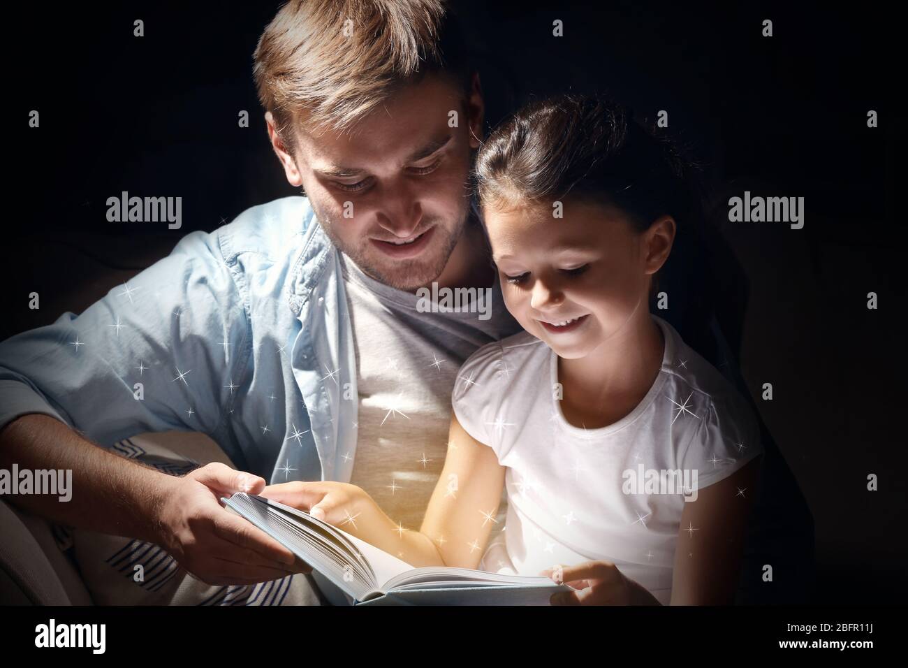 Vater mit Tochter Lesebuch auf dunklem Hintergrund Stockfoto