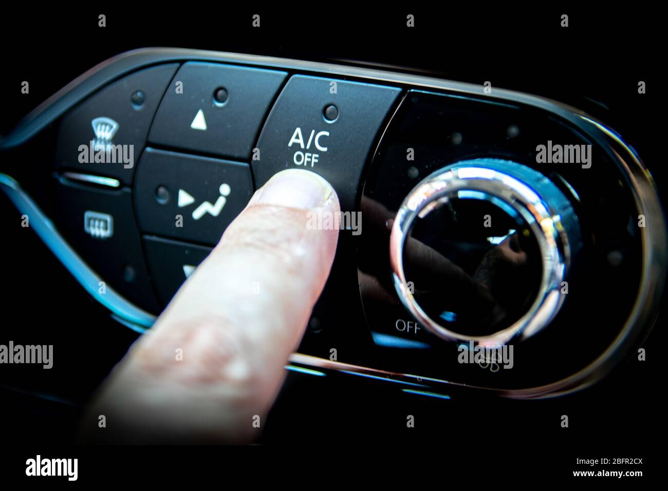 Ein Finger, der die A/C- oder Klimaanzeigetaste auf dem Armaturenbrett eines Autos drückt Stockfoto
