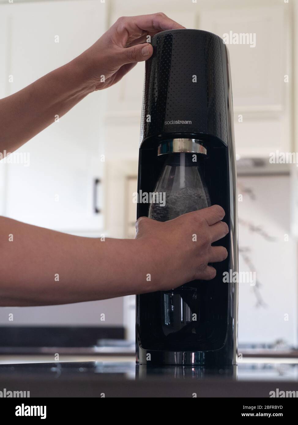 Latina Frau hält eine wiederverwendbare Sodastream Flasche, wie sie kohlensäurehaltige das Wasser enthält. Fotografiert in einer modernen Küche mit geringer Schärfentiefe. Stockfoto