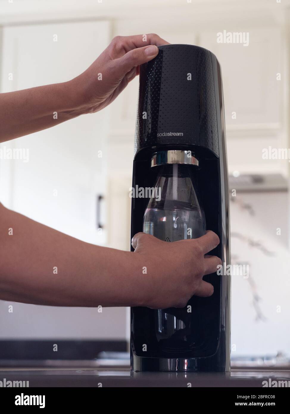 Latina Frau hält eine wiederverwendbare Sodastream Flasche, wie sie kohlensäurehaltige das Wasser enthält. Fotografiert auf Augenhöhe in moderner Küche. Stockfoto