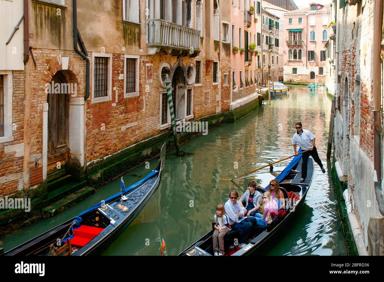 Zwei Gondeln, die in einem kleinen Seitenkanal vorbeifahren, während die Familie, die in einem reitet, die umliegenden Gebäude betrachtet. Venedig, Italien NMR Stockfoto