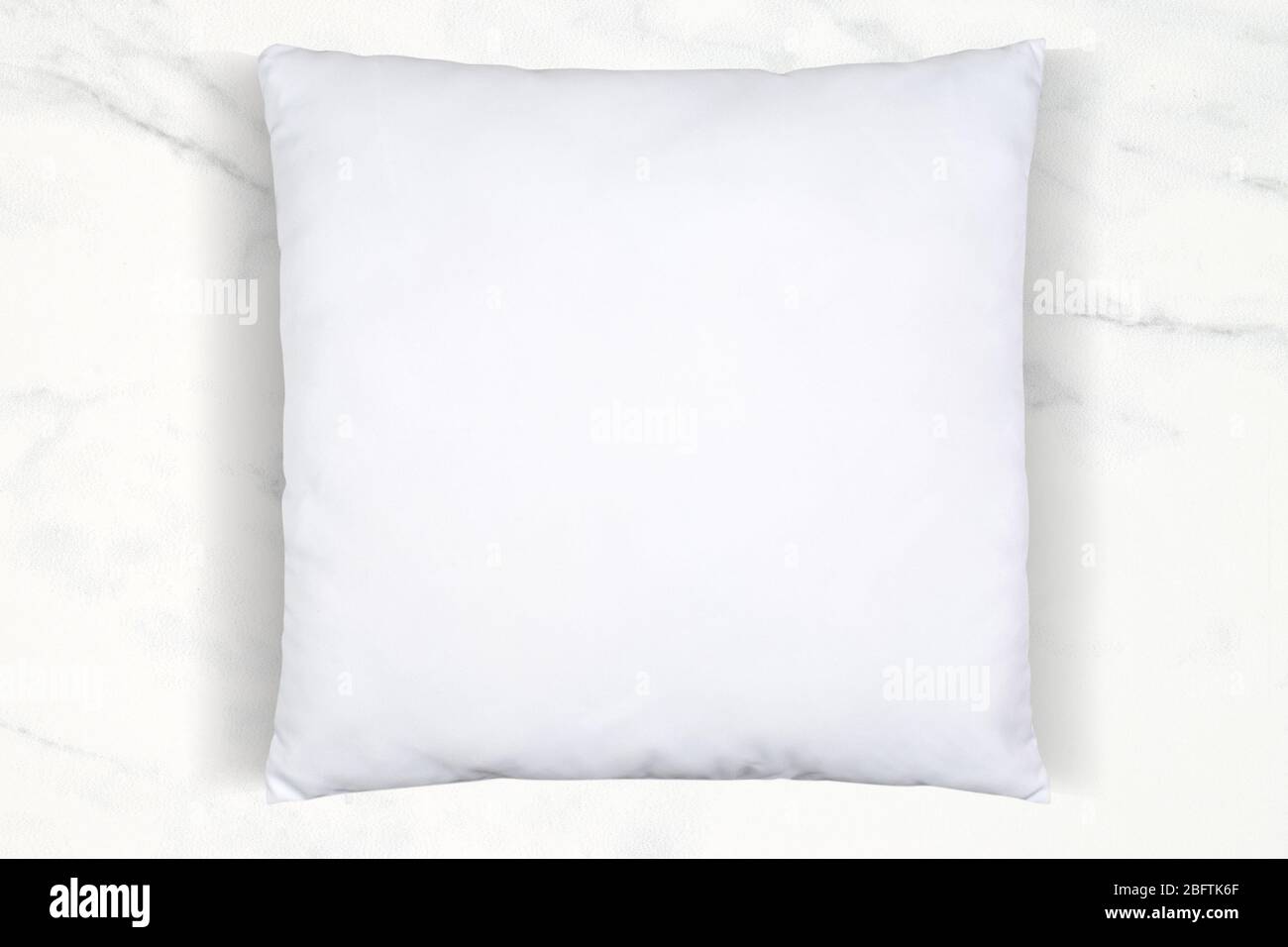 Ein weiches weißes Kissen mit Überwurf, das auf einem luxuriösen weißen Marmorhintergrund chillend ist. Viel Platz für Ihr eigenes Design in diesem Stehkragen mit Kissen. Stockfoto