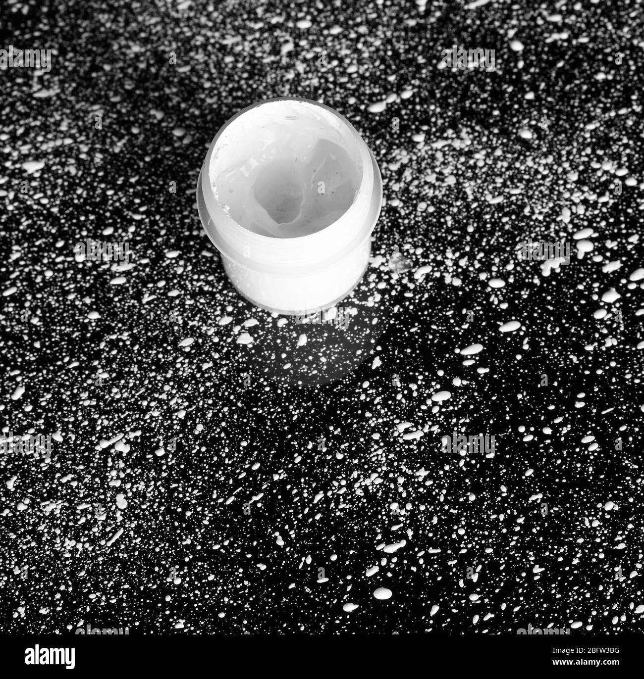 Glas mit weißem Gouache auf schwarzem Hintergrund, mit weißer Farbe Nahaufnahme bespritzt Stockfoto