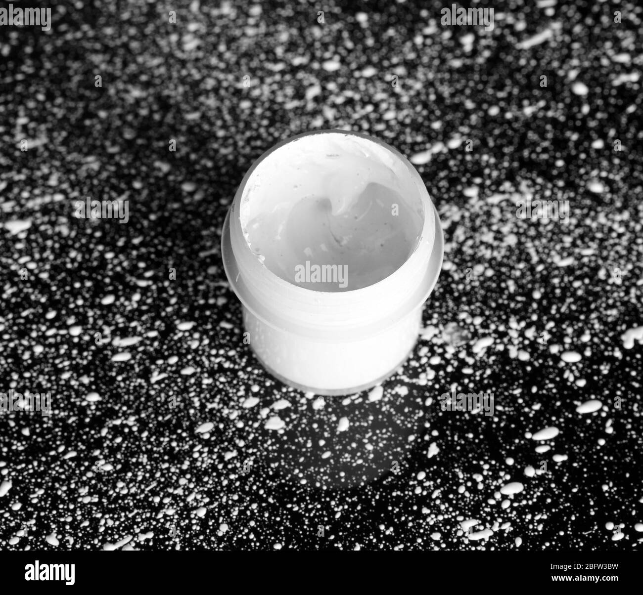 Glas mit weißem Gouache auf schwarzem Hintergrund, mit weißer Farbe Nahaufnahme bespritzt Stockfoto