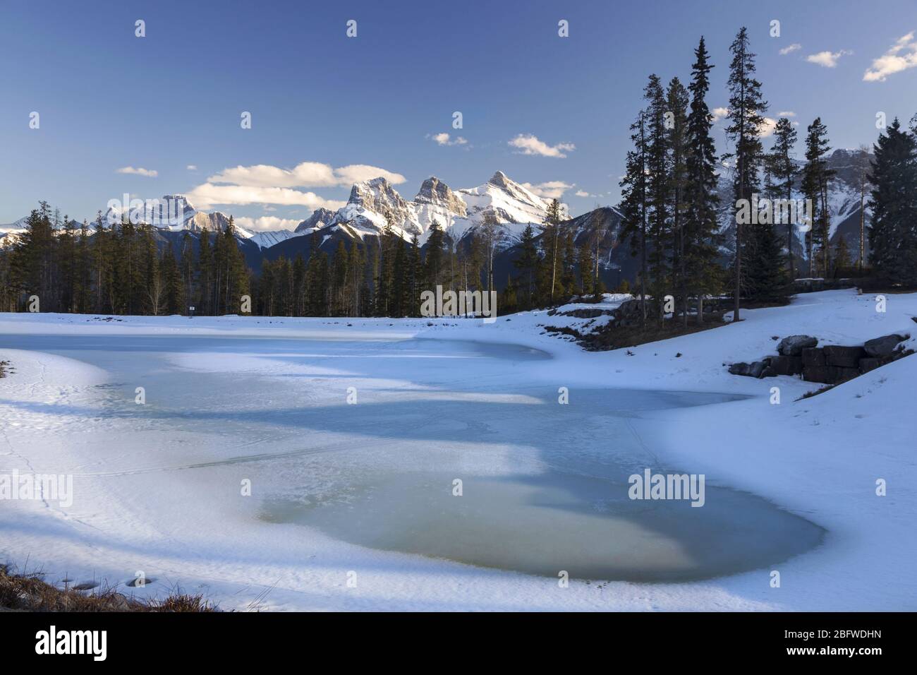 Gefrorener See und ferne verschneite Rocky Mountain Peaks Landschaft im frühen Frühling. Bow Valley, Canmore, Alberta, Kanada Stockfoto