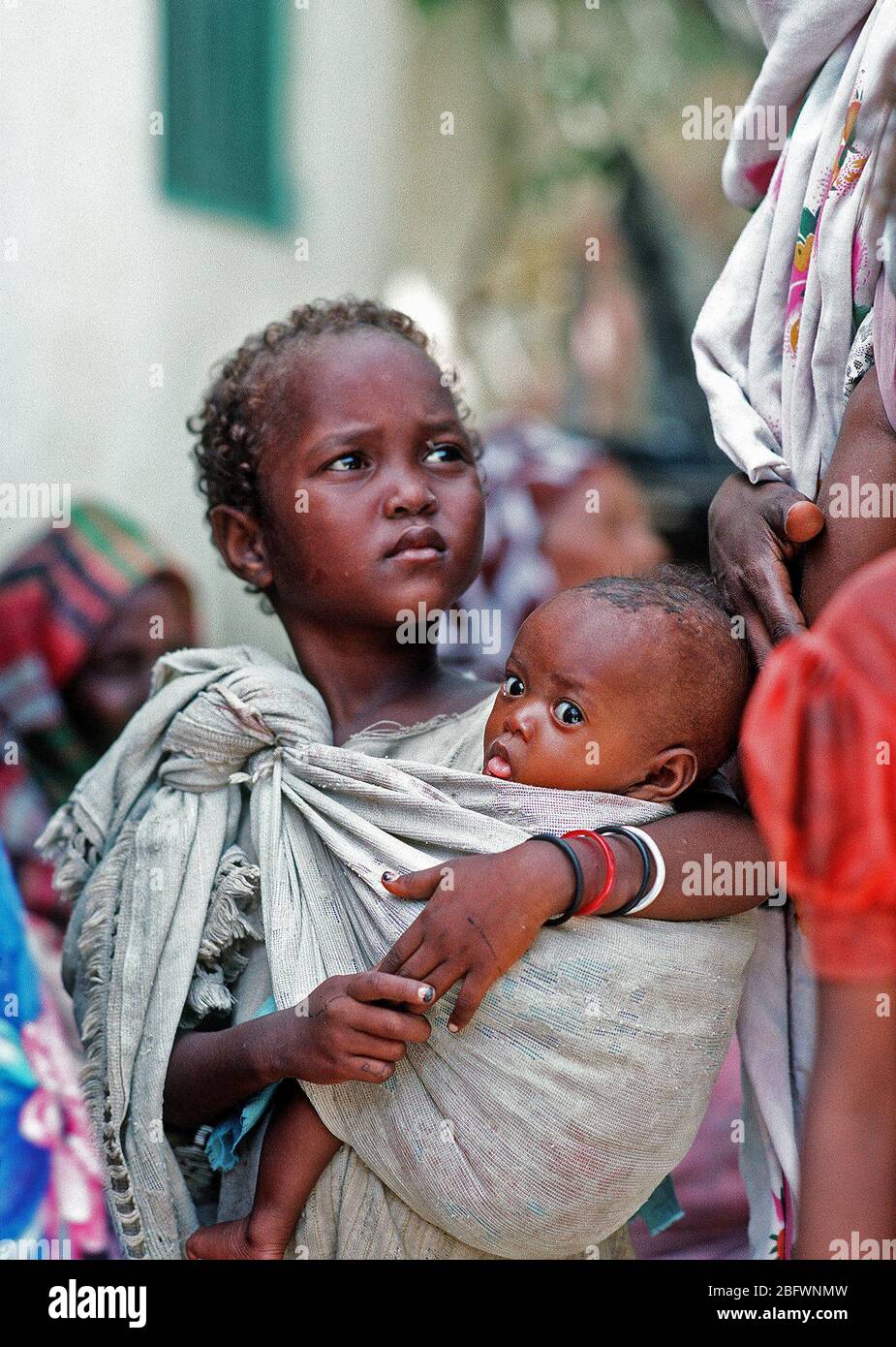 1993 - eine somalische Mädchen hält ein Kind während der Wartezeit durch ein Navy corpsman untersucht werden. Bekämpfung Service Support Abteilung 15 (CSSD-15) ist die Durchführung einer medizinischen civic Aktionsprogramm in den Straßen der Stadt während der multinationalen Entlastung Bemühung Operation Restore Hope. Stockfoto