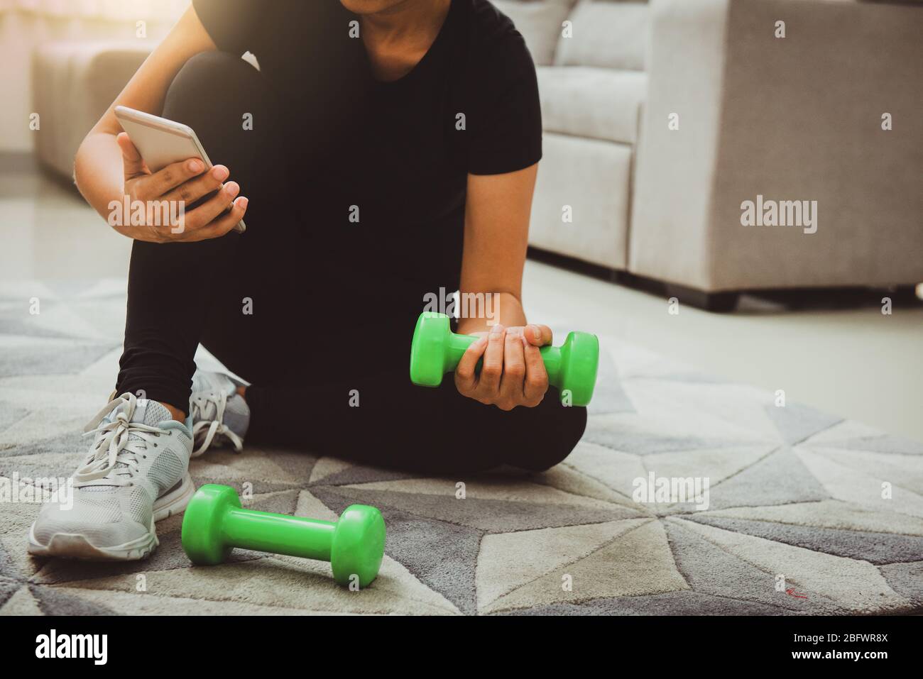 Eine sportliche Frau, die beim Training zu Hause im Wohnzimmer das Smartphone nutzt. Online Personal Trainer oder auf dem Handy.Sport und Erholung Konzept.adv Stockfoto