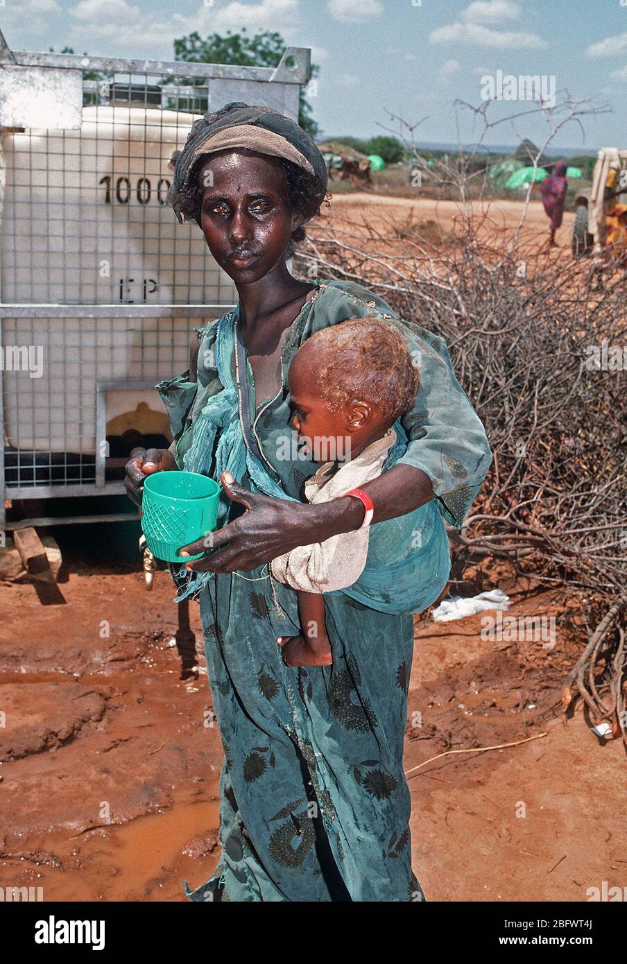 1993 - ein Somalischer Flüchtling Frau hält Ihr Kind, wie Sie in der Nähe ein Wasserspender stand auf einer Notfallstation Einrichten während der Operation Restore Hope Hilfsmaßnahmen (Badera Somalia) Stockfoto