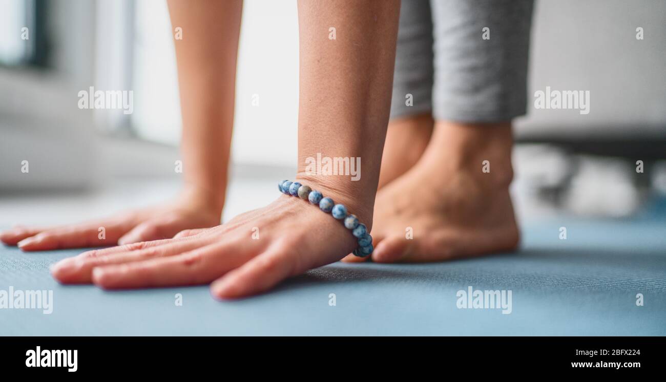 Yoga im Fitnessstudio - Yogalehrer Stretching in der Vinyasa Yoga-Klasse. Nahaufnahme der Hände mit blauem mala-Armband und barfuß Füße zu Hause. Stockfoto