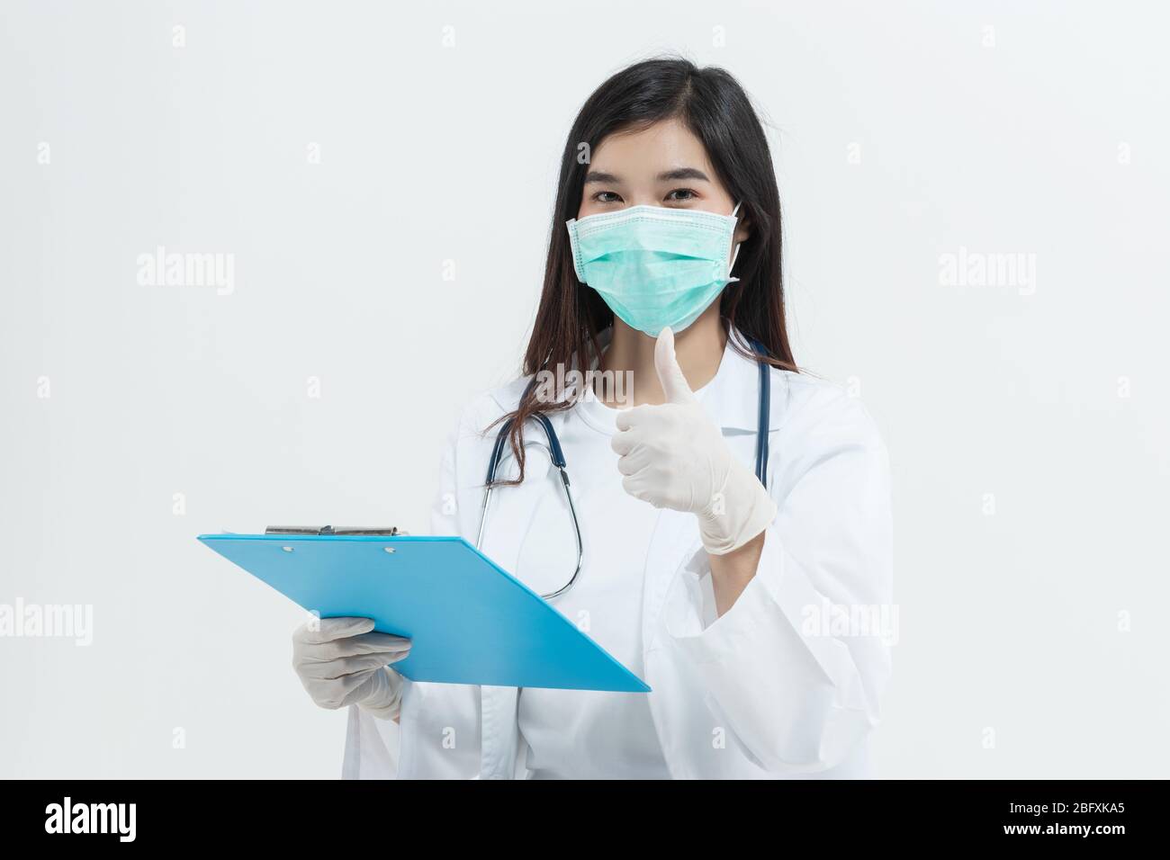 Junge asiatische Arzt Frau trägt Arzt Kleid Uniform Mantel , medizinische Maske und Stethoskop mit einem Clipboard glücklich und zeigt positive mit t Stockfoto