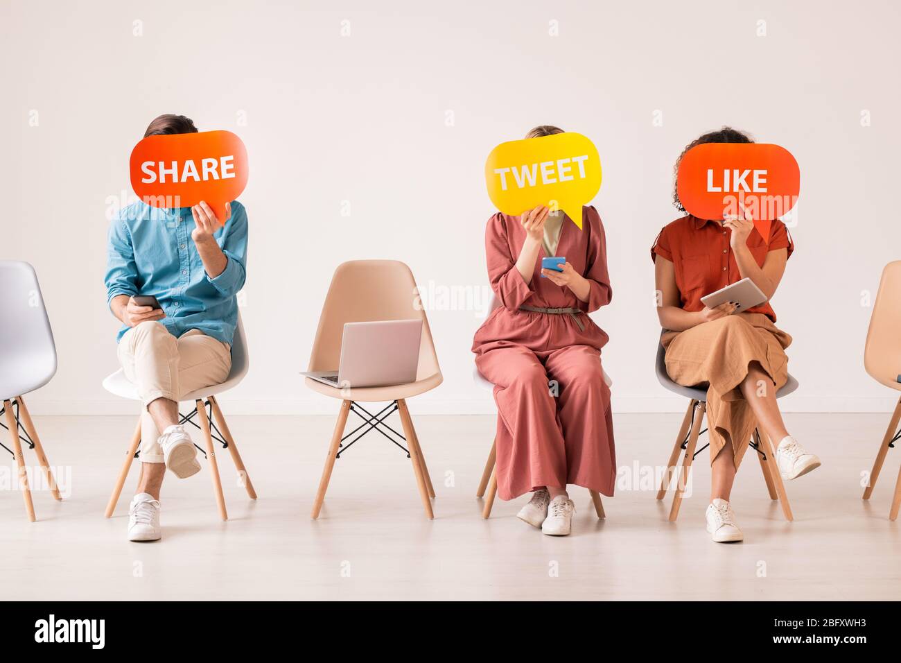 Unkenntlich erkennbare Social-Media-Nutzer sitzen mit Gadget in Reihe und versteckt Gesichter hinter bunten Tags mit Tweet, Like und Teilen Inschriften Stockfoto